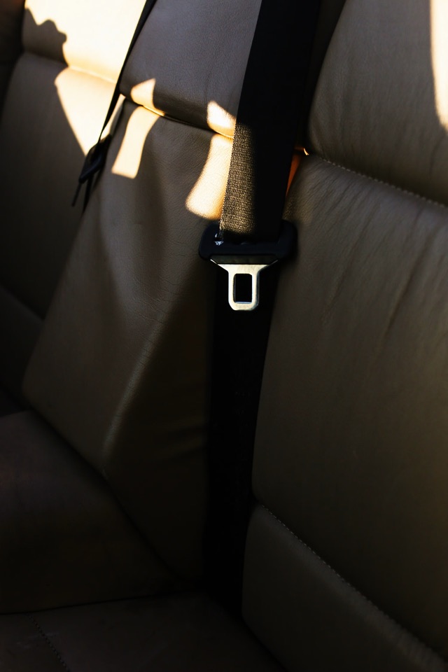 Seat belt webbing and latch plate resting against a light leather rear seat in low evening light
