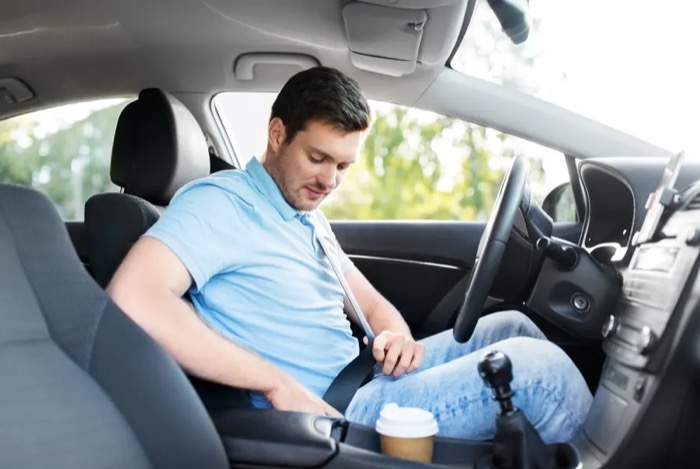 Driver in a light blue shirt fastening the seat belt in the front seat of a passenger car