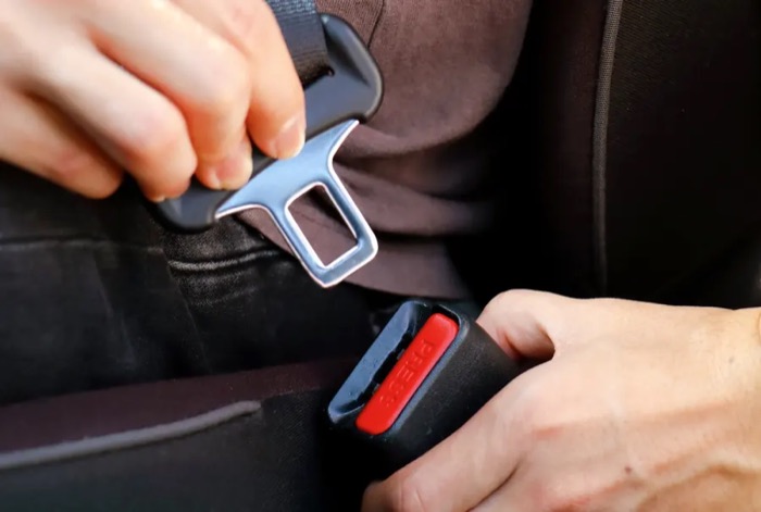Hands guiding a metal seat belt latch plate towards the red release button of a buckle receiver