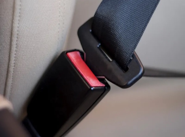 Seat belt latch plate positioned at the mouth of a buckle receiver, with the red release button visible
